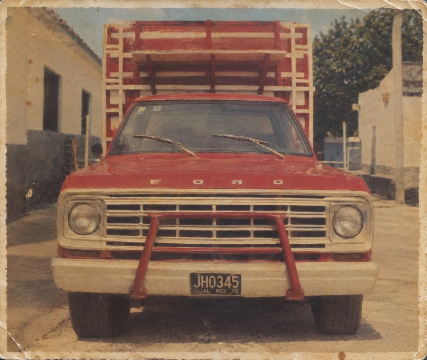 Fotografía antigua de la camioneta Ford roja con redilas con la que comenzó la empresa